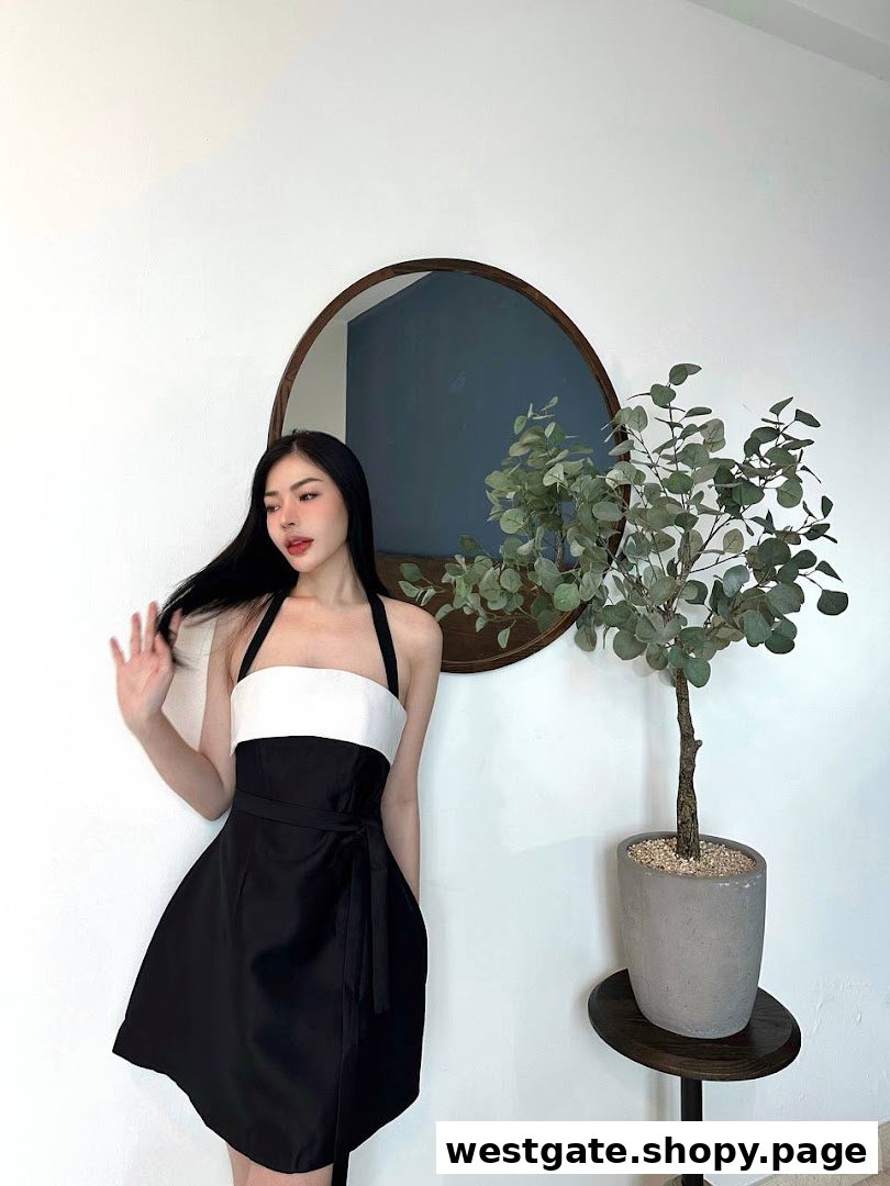A person models a black and white dress in a minimalist interior with a mirror and plant.