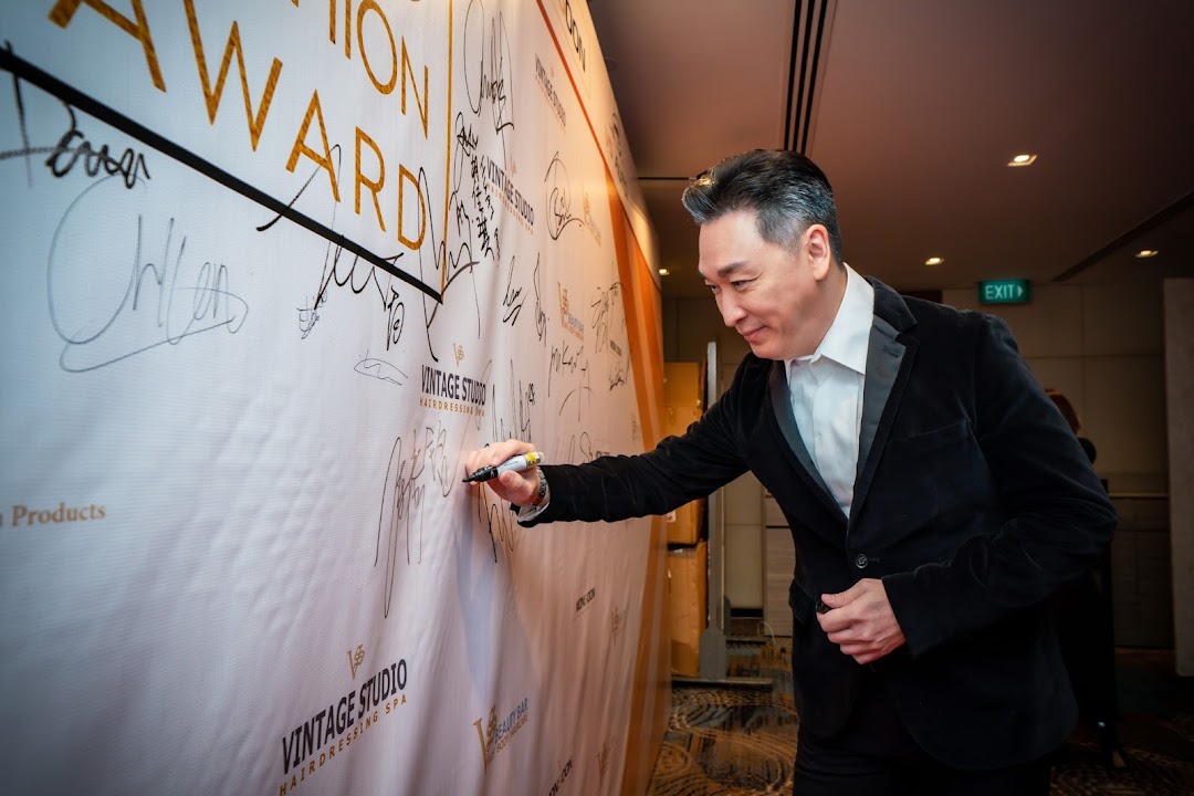 A man in a suit signs a banner featuring the 'Vintage Studio' logo and 'Hairdressing Spa'.