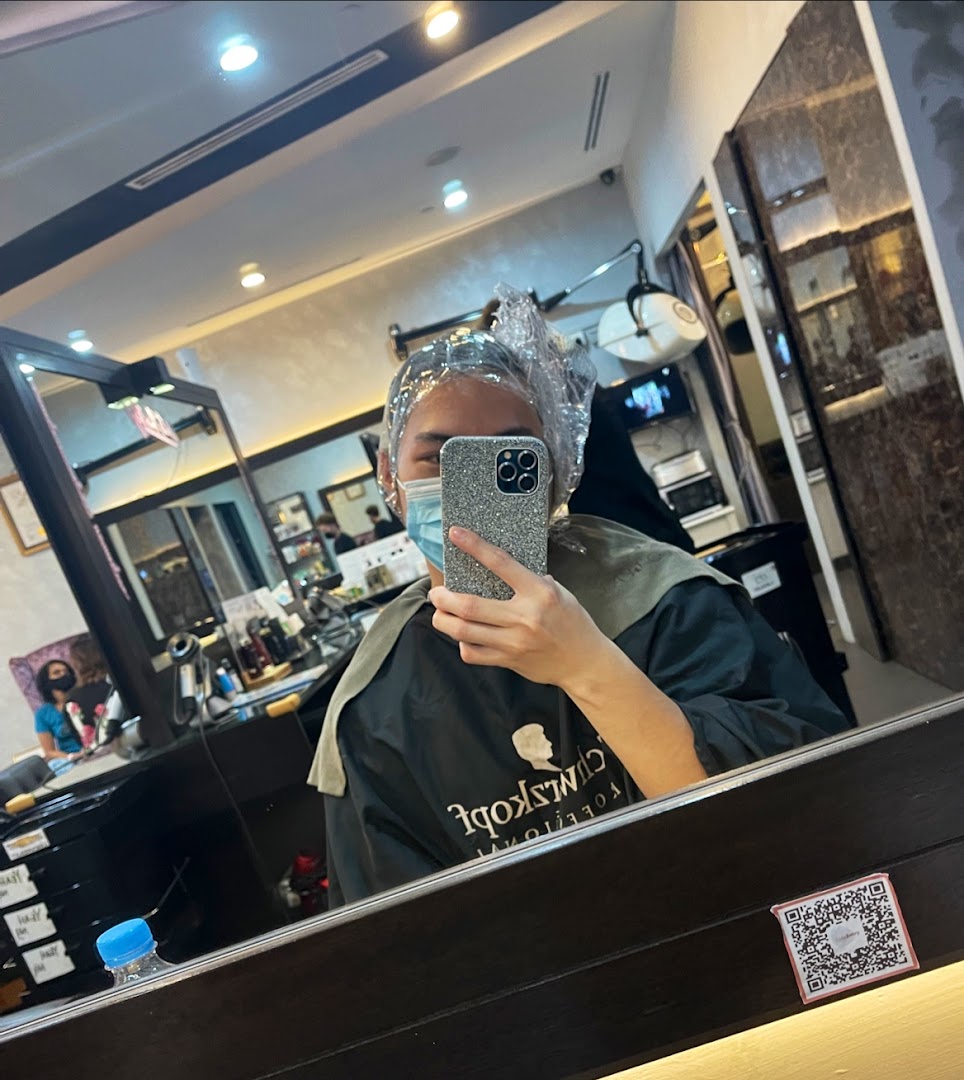 A customer in a salon chair, wearing a hair cap and mask, taking a mirror selfie during a hair treatment.