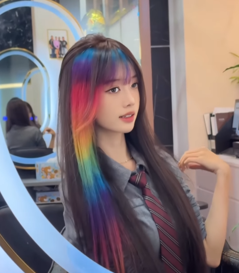A young woman showcasing vibrant rainbow-colored hair highlights in a salon setting.