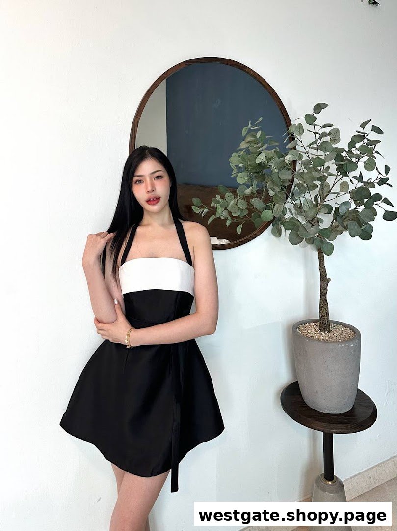 A woman in a black and white dress poses next to a plant and mirror in a stylish interior.