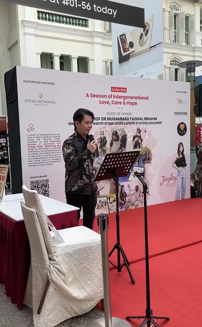 A man speaks at an event with a backdrop promoting 'A Season of Intergenerational Love, Care & Hope' and featuring Vintage Studio.