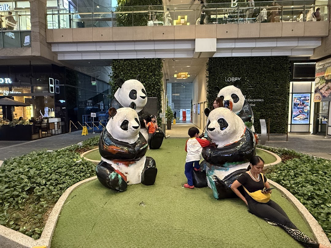 An outdoor mall area featuring large, colorful panda statues, surrounded by greenery and mall visitors.