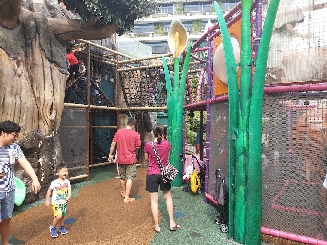 Children and adults enjoy a multi-level indoor playground with a treehouse theme and large plant decorations.
