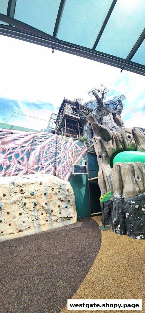 An outdoor adventure play area featuring a climbing wall and a multi-level treehouse structure.