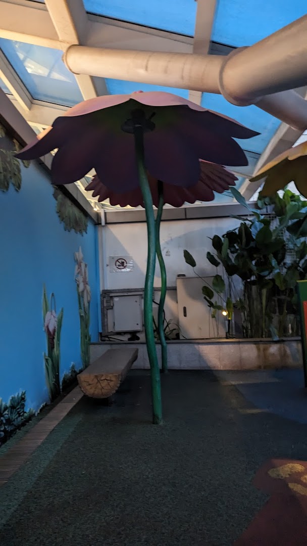 A whimsical indoor play area featuring oversized flower decorations, a log bench, and painted nature scenes.
