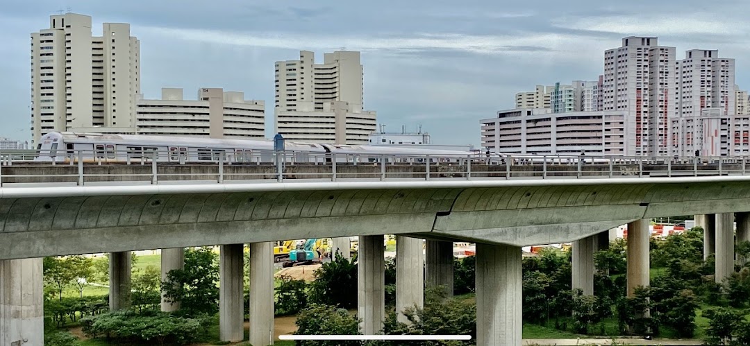 An elevated train track with a train passing, surrounded by residential buildings and lush greenery.