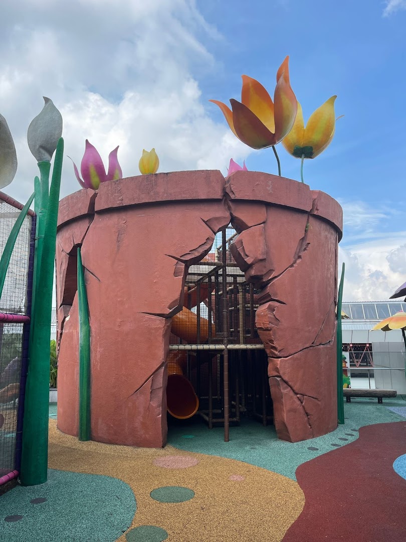 A large, cracked flower pot play structure with slides and colorful giant tulips under a blue sky.