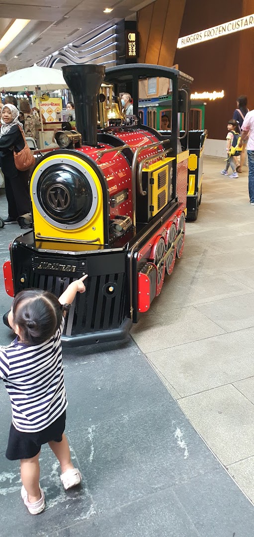 A child points excitedly at a vibrant red and yellow mini-train ride inside a bustling shopping mall.