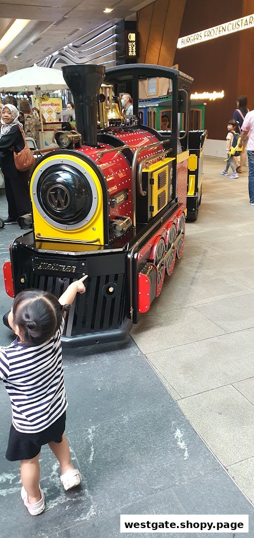 A child points excitedly at a vibrant red and yellow mini-train ride inside a bustling shopping mall.