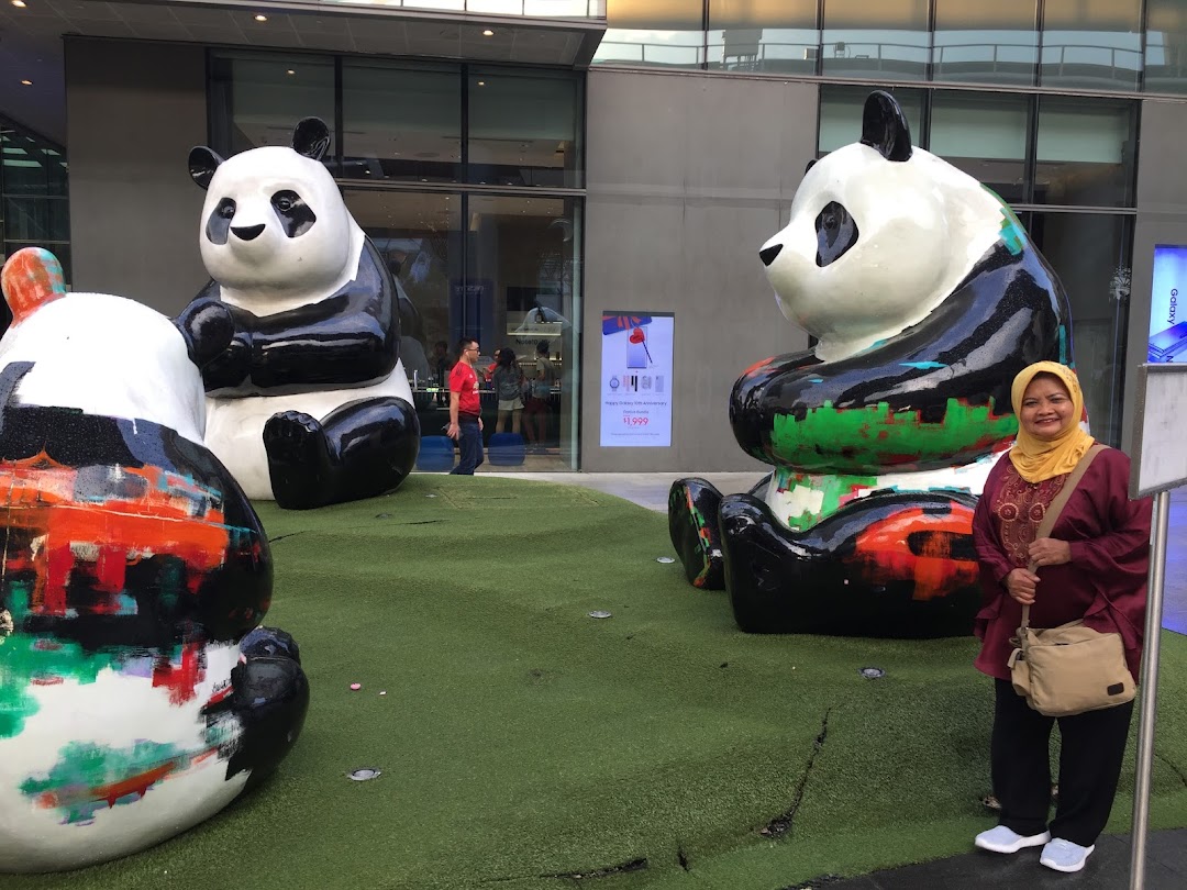 Large, colorful panda statues on artificial grass outside a modern building with a woman smiling.