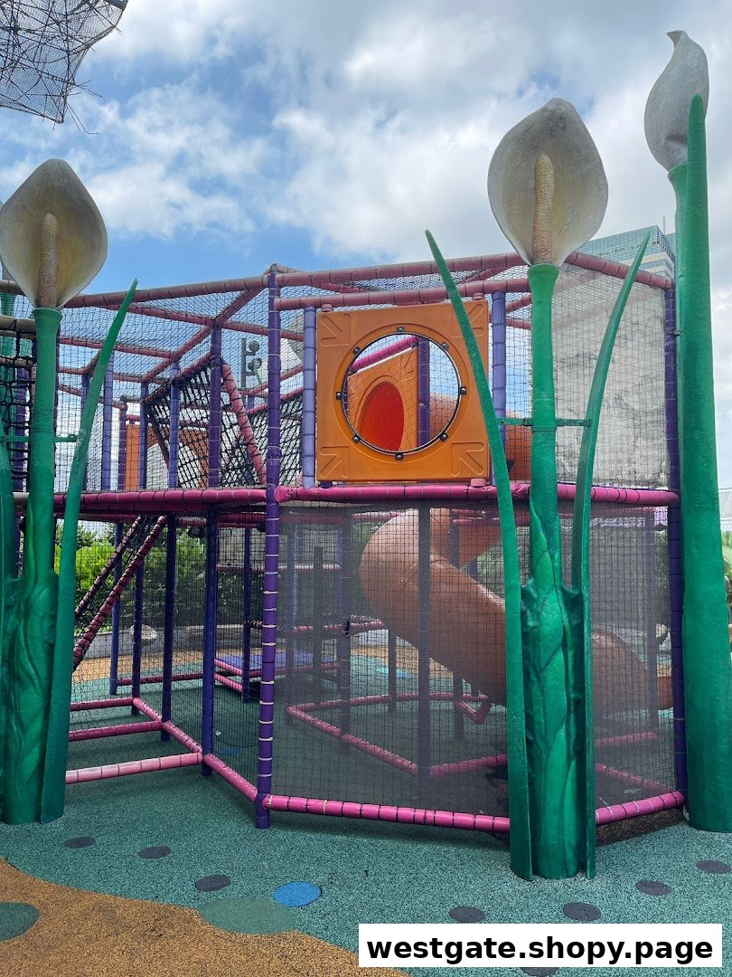 A vibrant outdoor playground with colorful structures, slides, and climbing nets, surrounded by large plant sculptures.