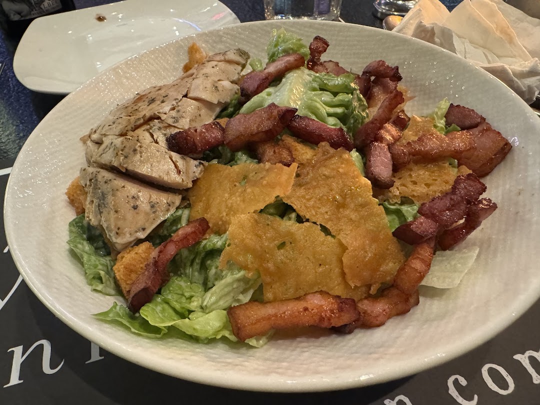 A close-up of a delicious Caesar salad with grilled chicken, crispy bacon, and parmesan crisps.