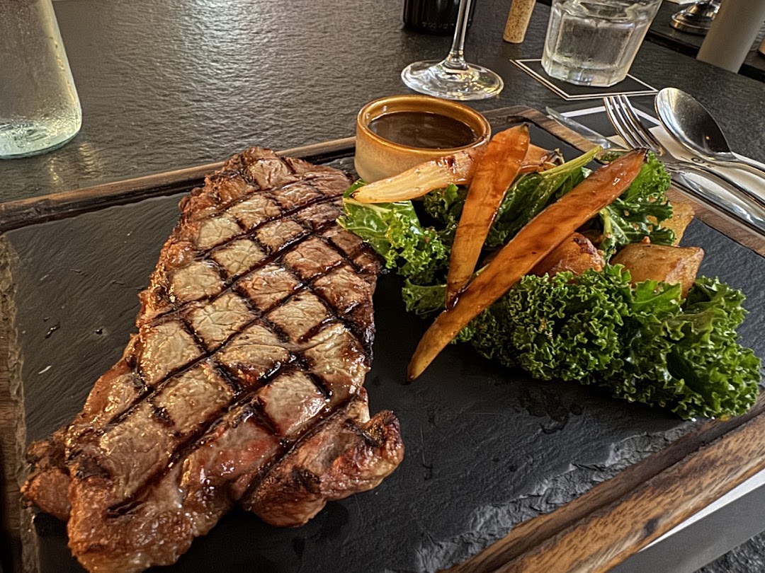 A perfectly grilled steak served with roasted vegetables and a side of sauce on a dark slate board.