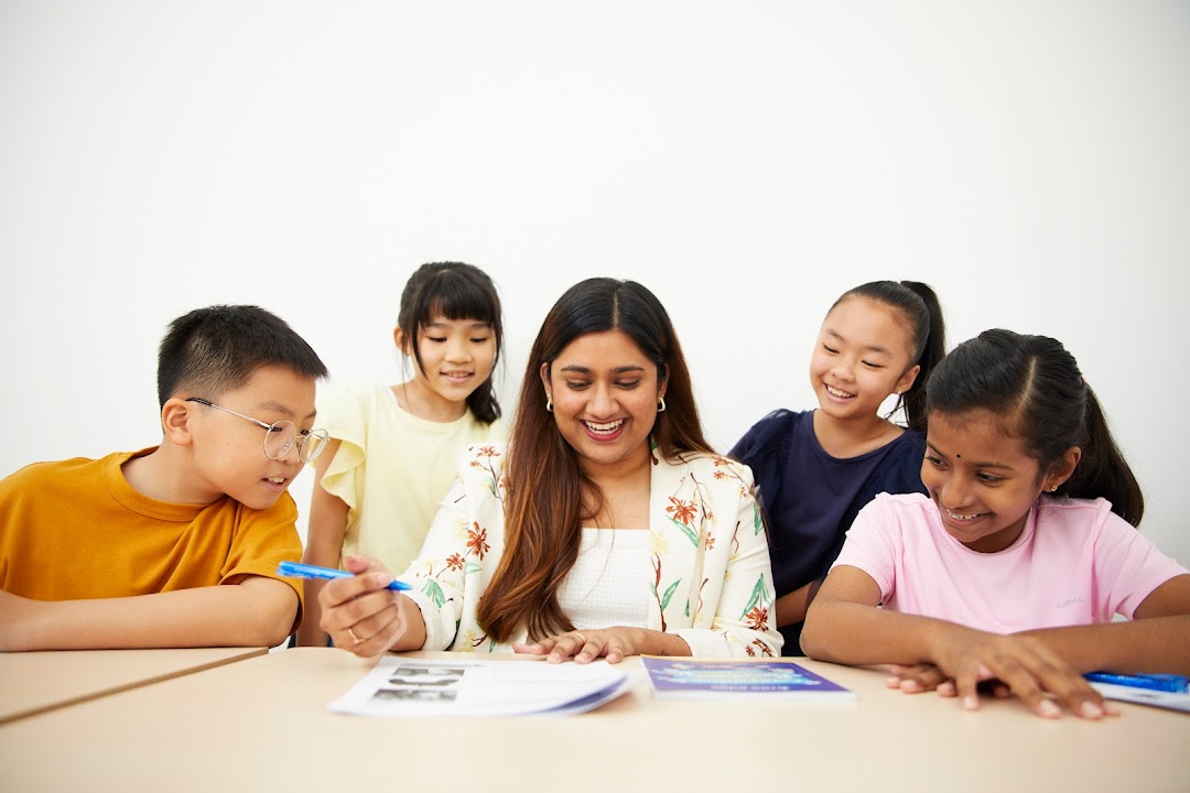A teacher smiles while engaging with four diverse students at a learning table.