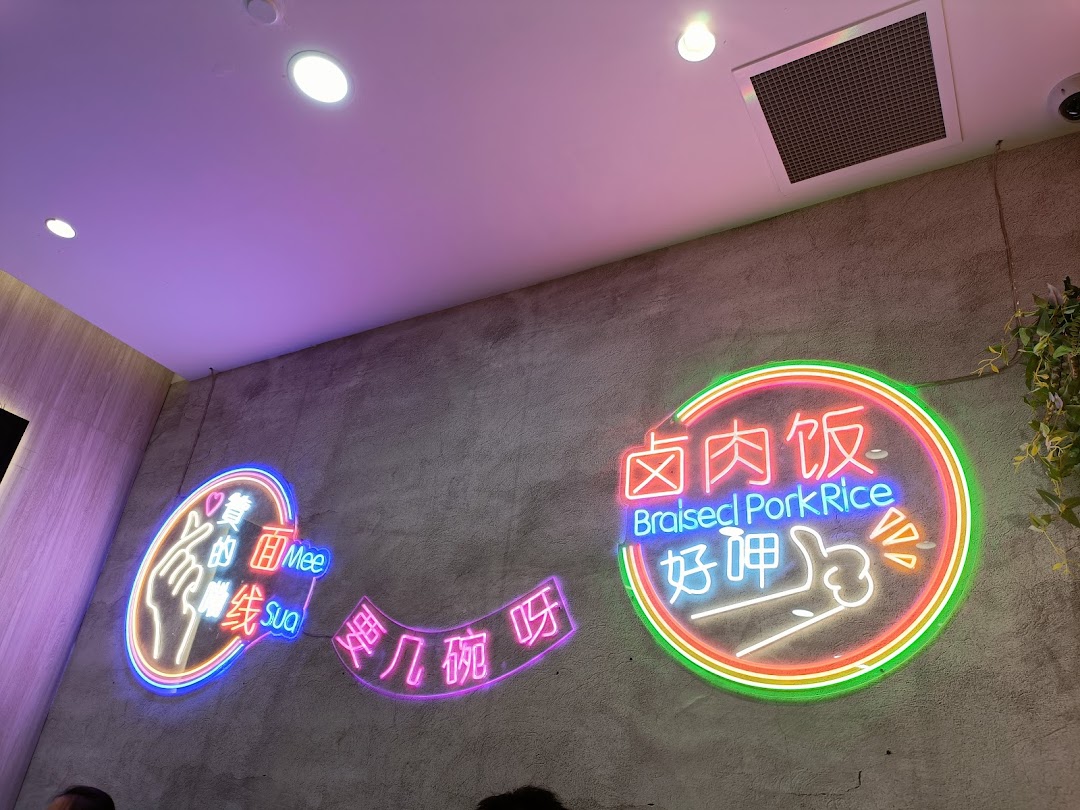 Vibrant neon signs on a textured wall, featuring 'Braised Pork Rice' and 'Mee Sua' in a modern setting.
