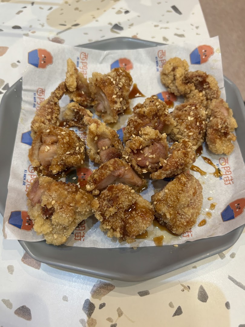 A close-up of crispy, golden-brown fried chicken pieces with sesame seeds and sauce on a plate.