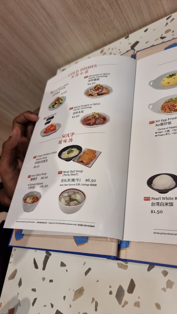 A person's hand holding open a menu displaying various Taiwanese cold dishes, soups, and rice options.