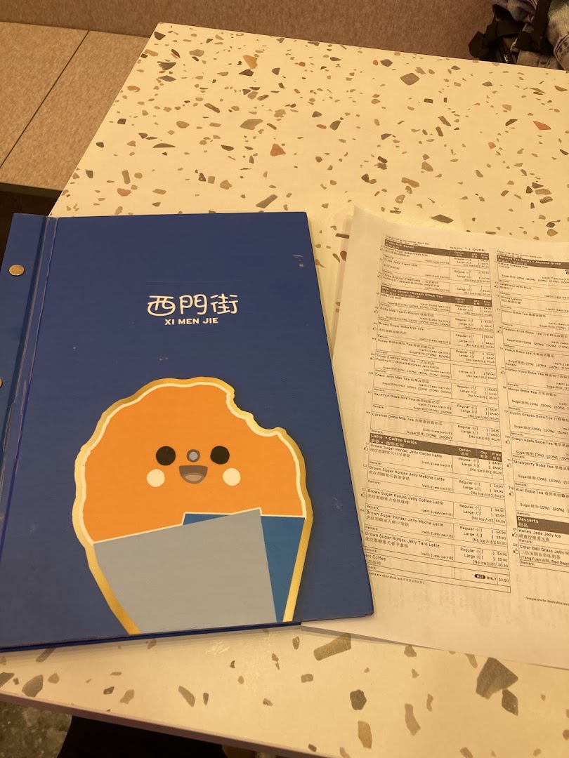 A blue menu book and a printed menu sheet for Xi Men Jie on a speckled table.
