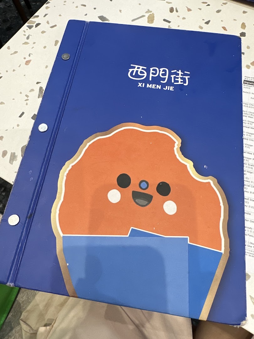A blue menu binder for Xi Men Jie restaurant featuring a cute cartoon character on its cover.