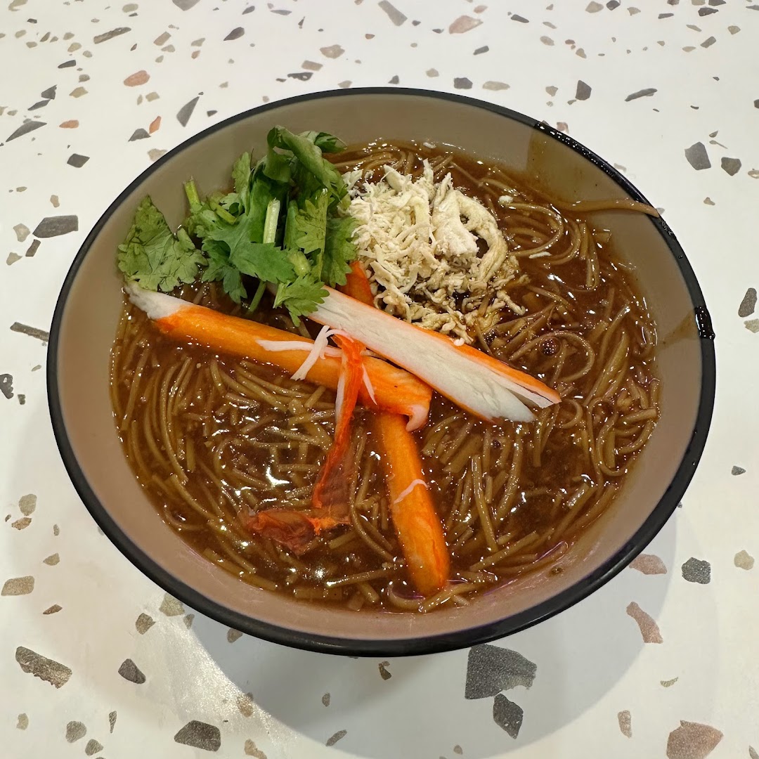A close-up of a bowl of Taiwanese vermicelli with crab sticks, shredded meat, and cilantro.