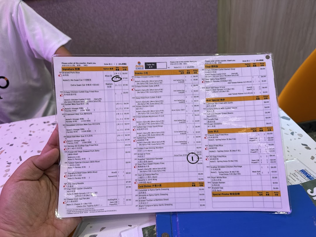 A close-up view of a laminated menu from Xi Men Jie, featuring various Taiwanese dishes and prices.