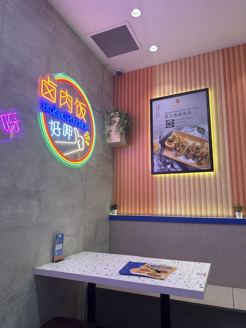 A modern interior shot of Xi Men Jie featuring a neon sign, a dining table, and a promotional food poster.