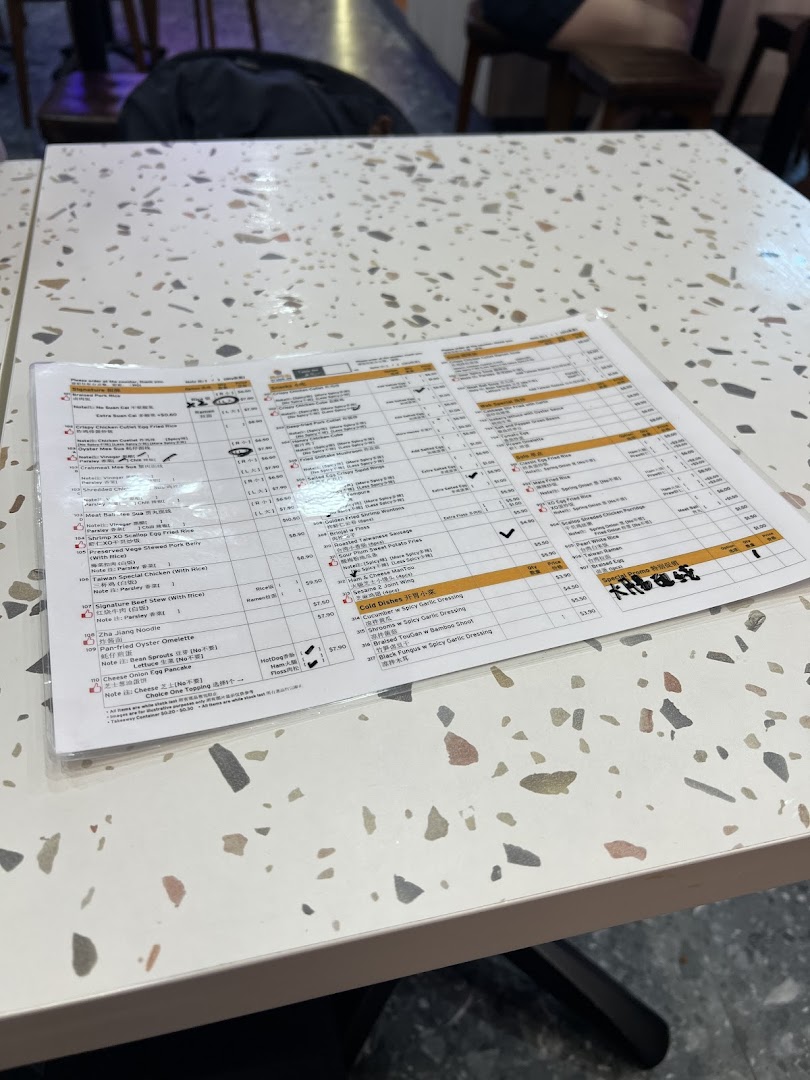A laminated menu displaying Taiwanese dishes on a speckled white table.