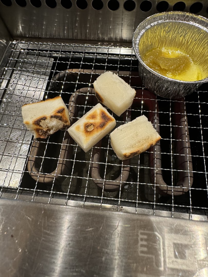 Grilled mochi or rice cakes on a personal yakiniku grill with a dipping sauce.