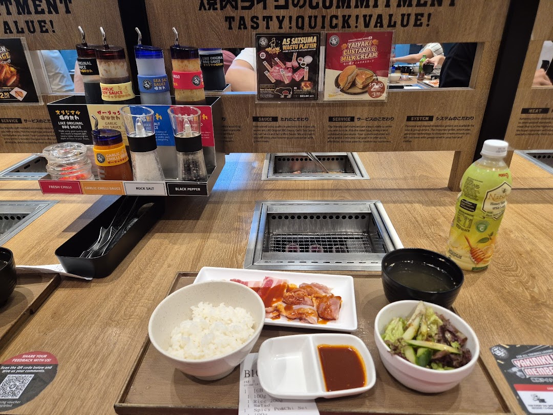A personal yakiniku grill station with raw meat, rice, salad, sauces, and a drink, ready for grilling.