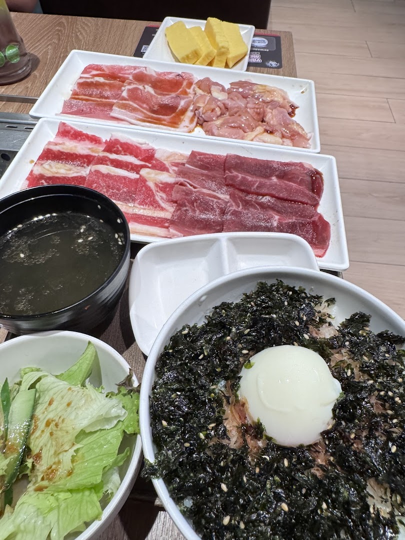 A table laden with raw meats for grilling, a rice bowl, salad, and soup at Yakiniku Like.