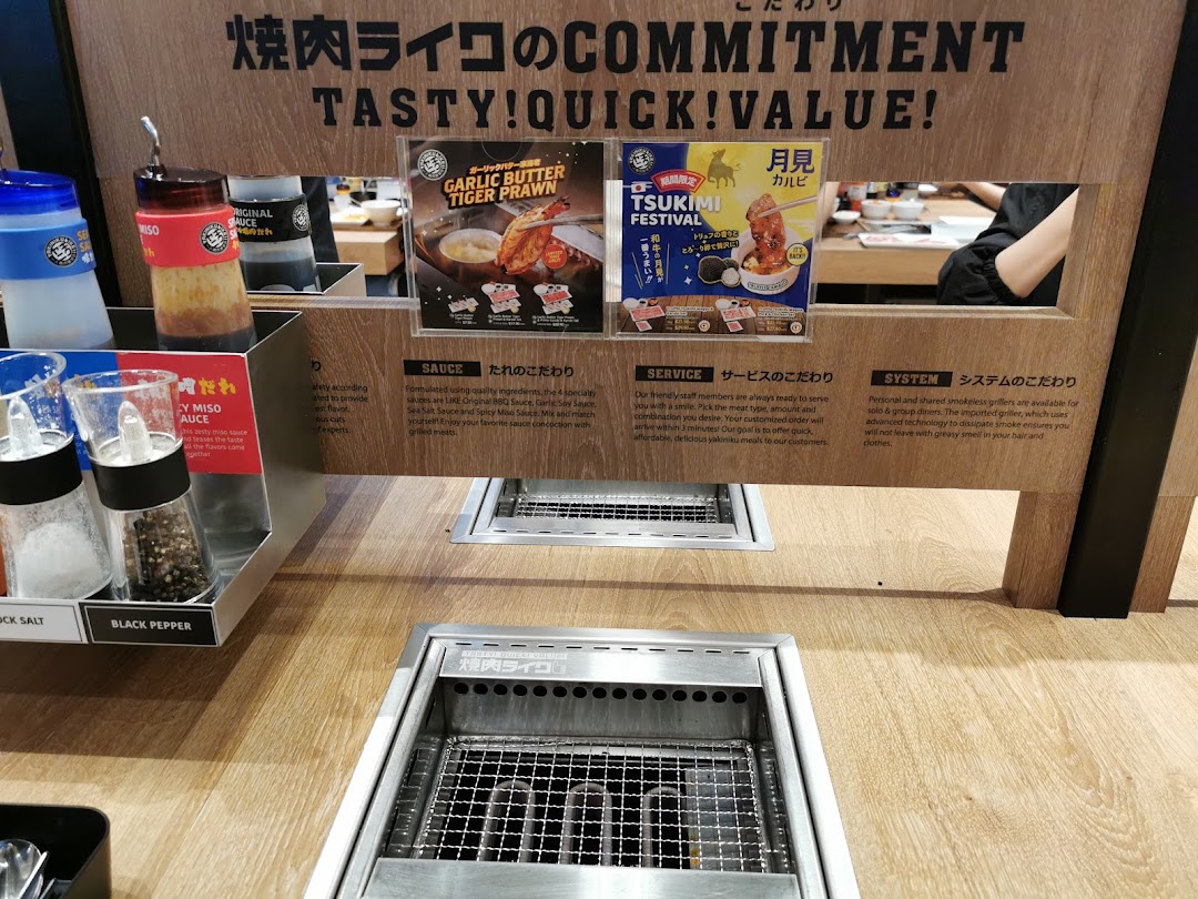 A Yakiniku Like dining station featuring a personal grill, condiments, and promotional posters.