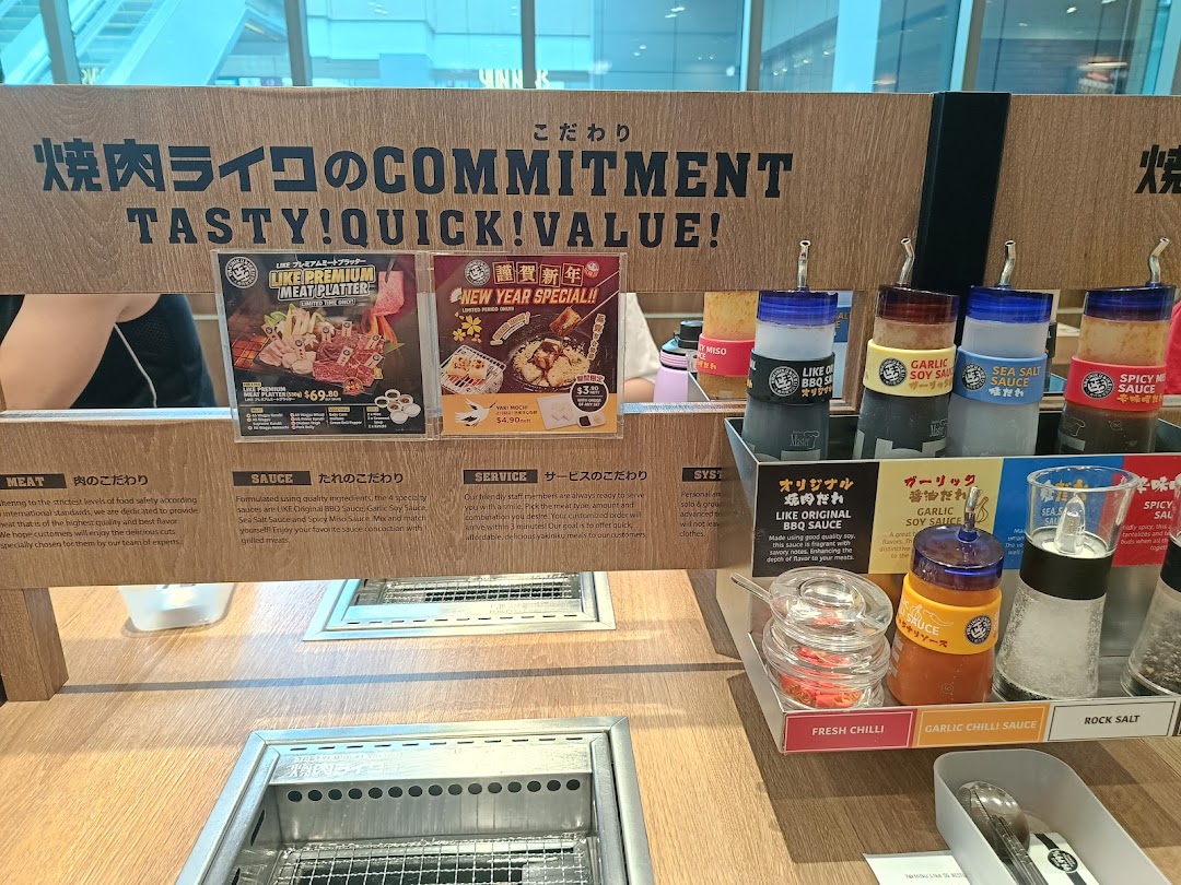 A restaurant table with a built-in grill, various sauces, and promotional posters for meat platters and specials.