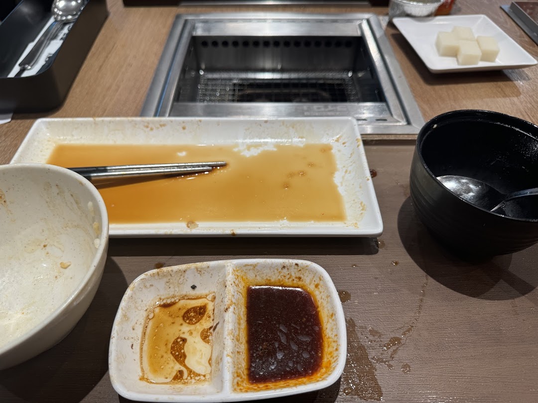 A table at Yakiniku Like with used dishes, sauces, and a grill after a satisfying meal.