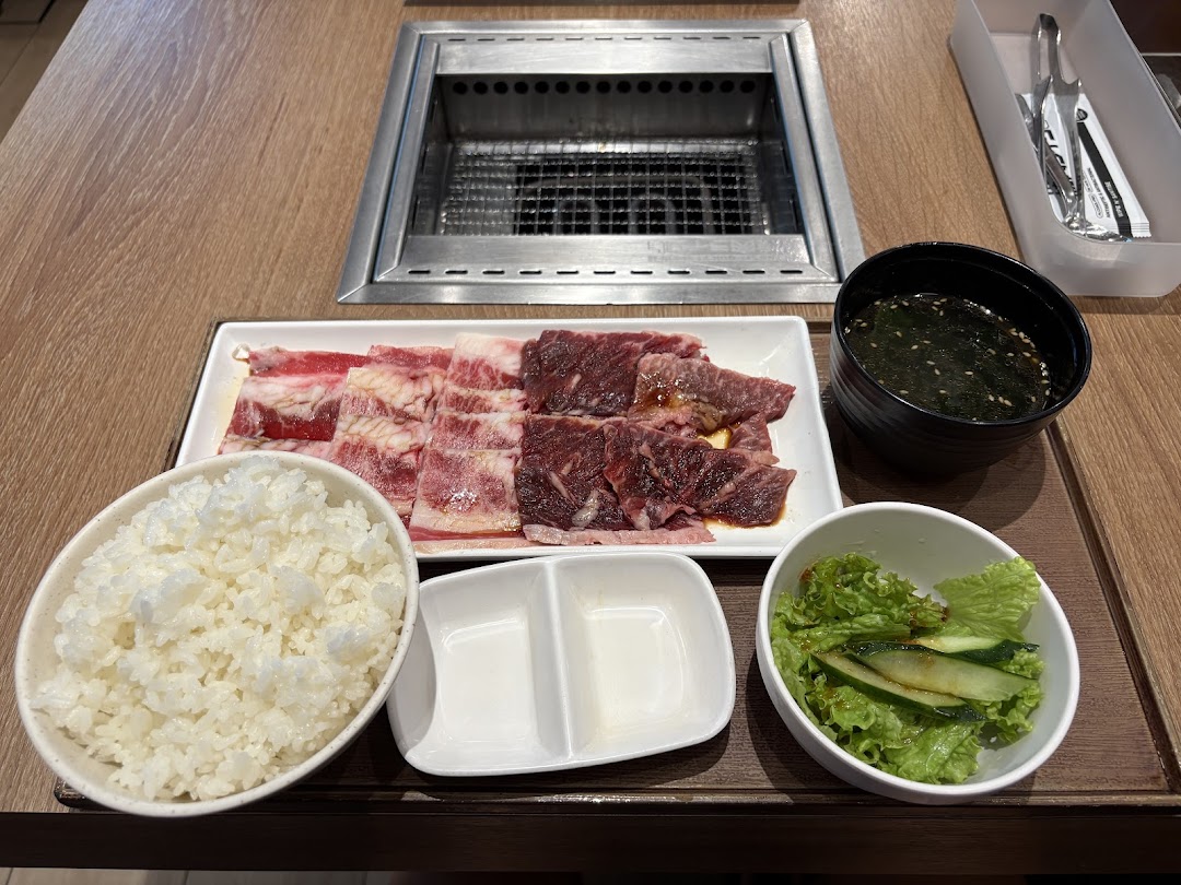A delicious Yakiniku meal set with raw beef, rice, soup, and salad on a table with a grill.