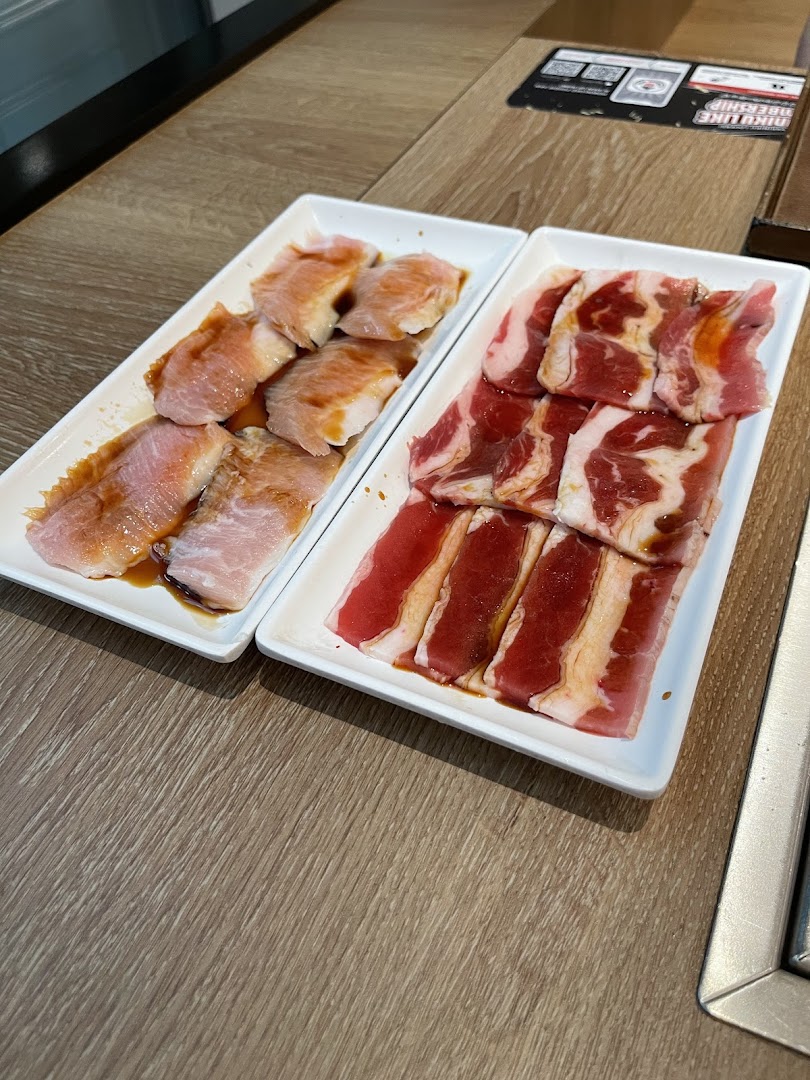 Two plates of raw, marinated meat, likely beef and pork, on a wooden table.
