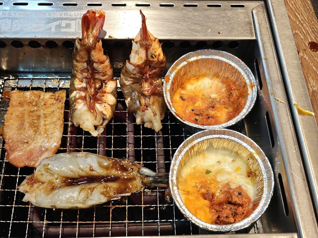Assorted seafood and meat grilling on a yakiniku grill, with cheesy side dishes in foil cups.