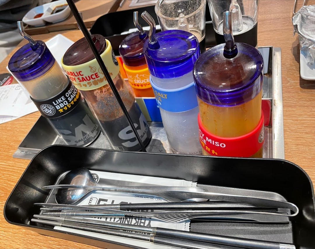 A close-up of various sauces, condiments, and cutlery on a table at Yakiniku Like.