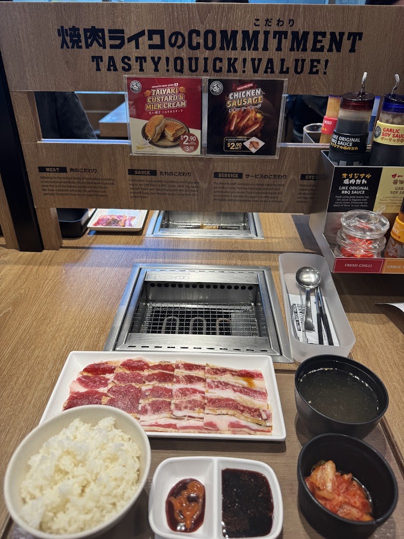A close-up of a Yakiniku Like dining setup with raw meat, rice, sauces, and a grill.