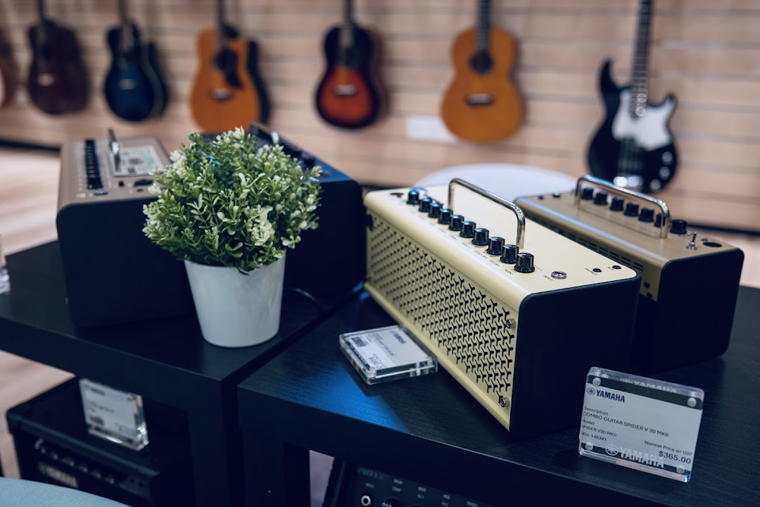 A display of Yamaha guitar amplifiers and a plant, with guitars visible in the background.