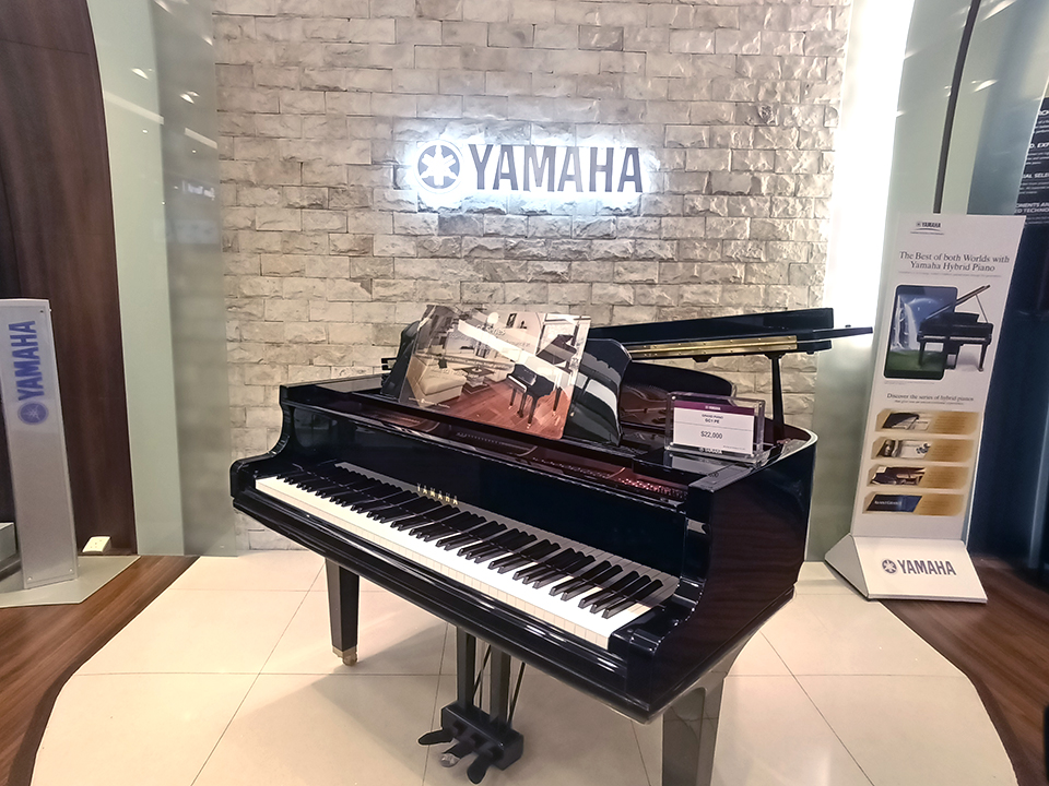 A sleek black grand piano displayed in a Yamaha Music Store, featuring a glowing logo.