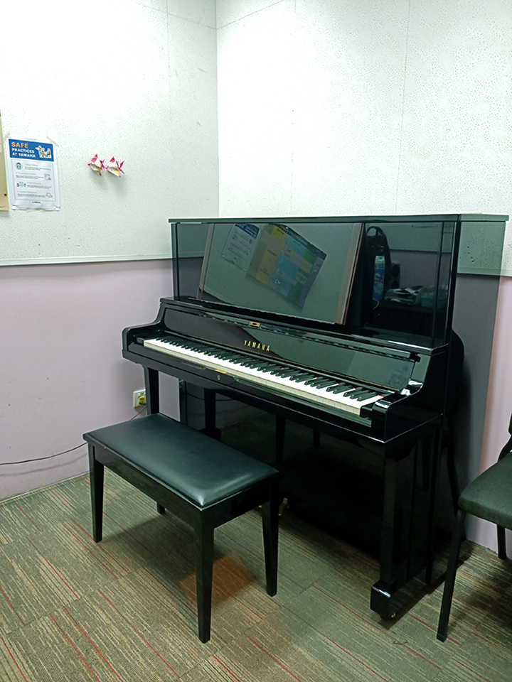 A black Yamaha upright piano with a bench in a music practice room.