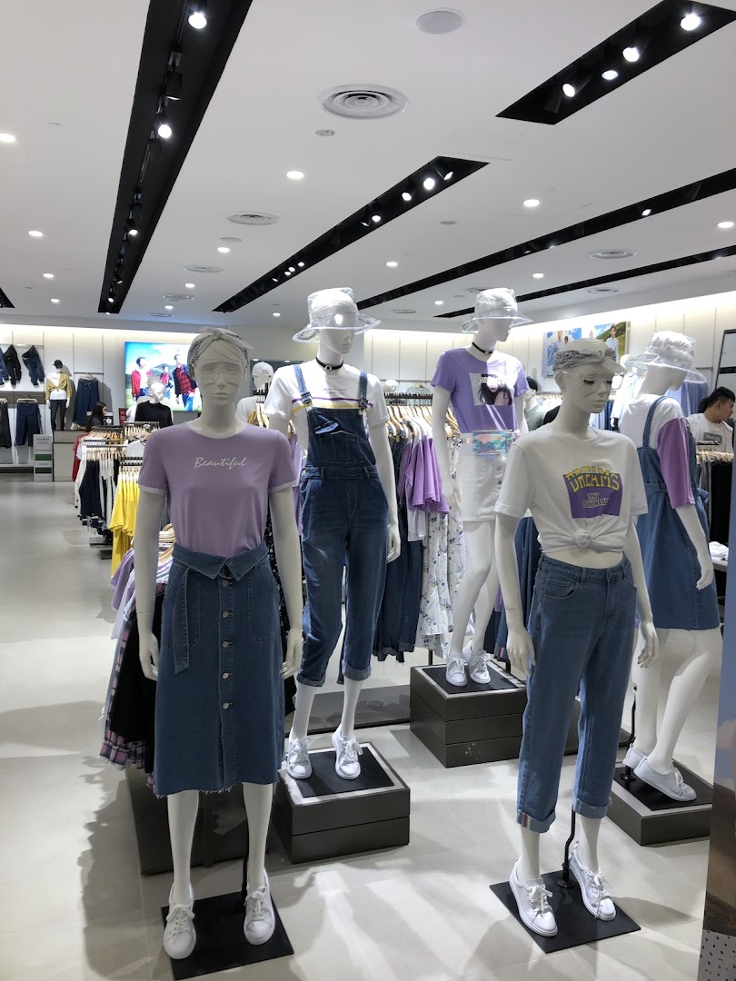 Mannequins display trendy casual wear, including denim and pastel tops, inside a bright clothing store.