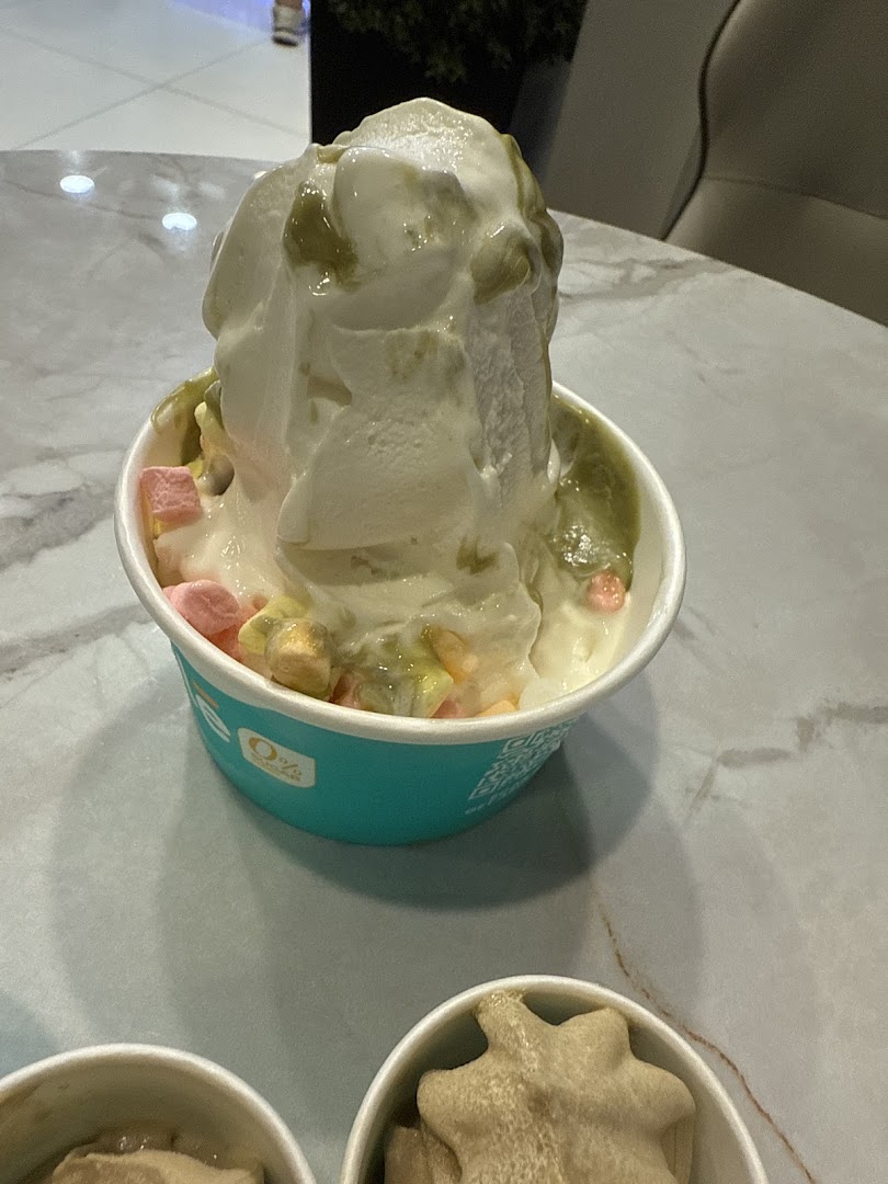 A close-up of a cup of frozen yogurt topped with marshmallows and green sauce on a table.