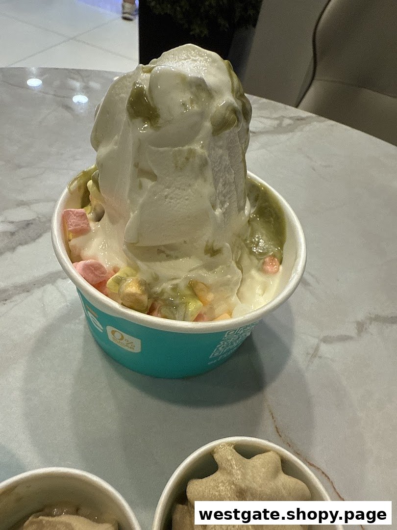 A close-up of a cup of frozen yogurt topped with marshmallows and green sauce on a table.
