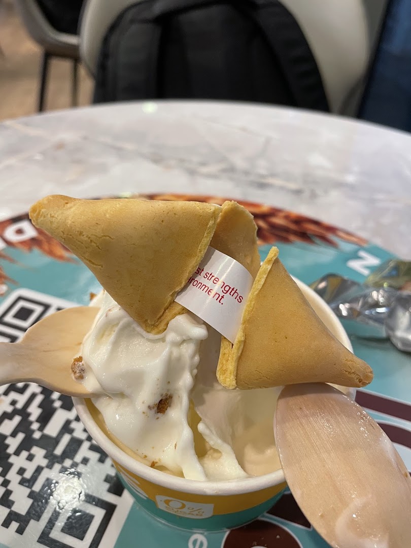 A cup of frozen yogurt topped with a fortune cookie and a wooden spoon.