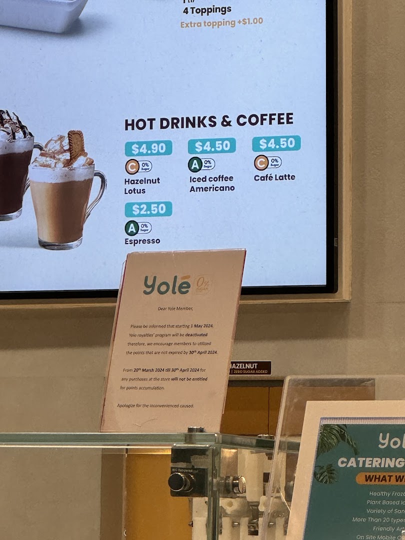 A digital menu board displaying hot drinks and coffee options with prices at Yolé, alongside a loyalty program update.