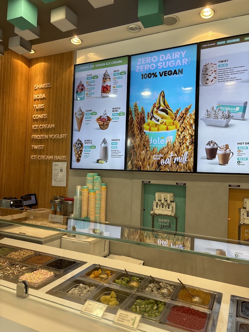 Interior view of Yolé Westgate, showcasing the frozen yogurt counter, toppings, and digital menu boards.