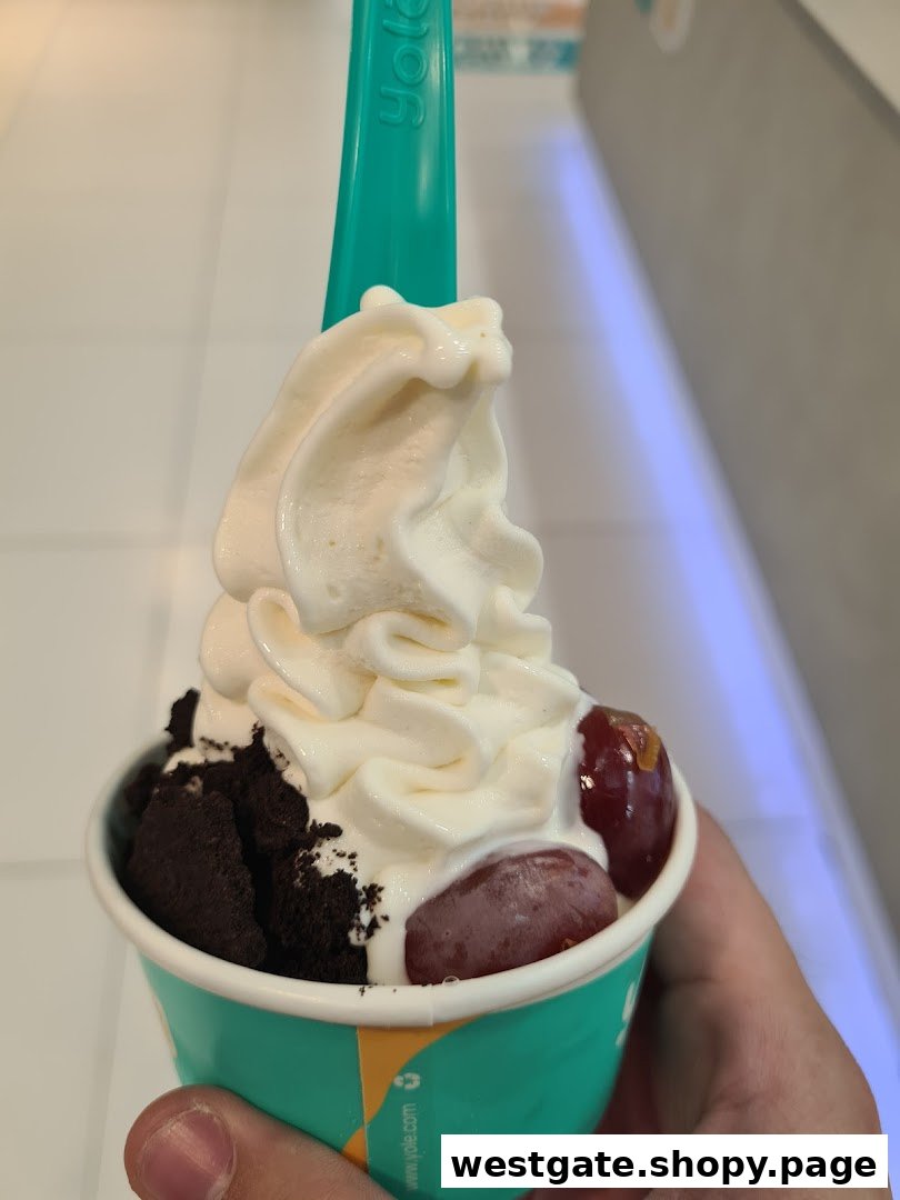 A hand holds a cup of Yolé frozen yogurt topped with creamy froyo, chocolate cookie crumbles, and fresh grapes.