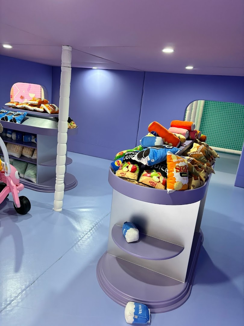 Interior view of Yooland featuring colorful plush food toys on display stands in a vibrant purple-themed room.
